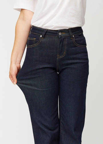 Das Model dehnt die tief dunkelblaue Denim jeans für Damen in der Farbe Midnights am Oberschenkel, um die Stretchqualität des Materials zu zeigen.