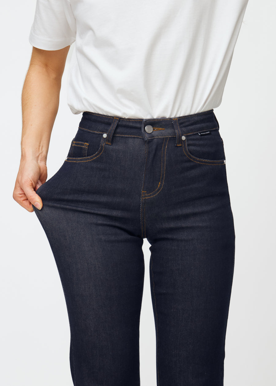 Das Model dehnt die tief dunkelblaue Denim jeans für Damen in der Farbe Midnights am Oberschenkel, um die Dehnbarkeit des Materials zu zeigen.
