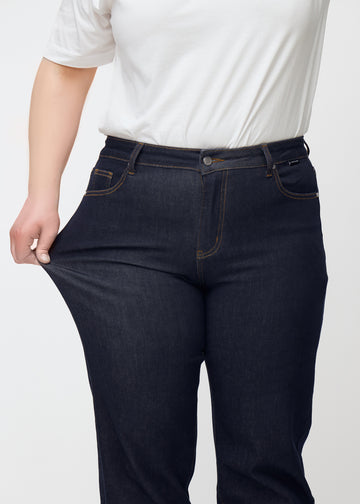 Das Plus-Size-Model dehnt die tief dunkelblaue Denim jeans für Damen in der Farbe Midnights am Oberschenkel, um die Dehnbarkeit des Materials zu zeigen.