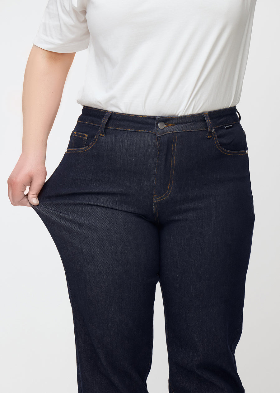 Das Plus-Size-Model dehnt die tief dunkelblaue Denim jeans für Damen in der Farbe Midnights am Oberschenkel, um die Dehnbarkeit des Materials zu zeigen.