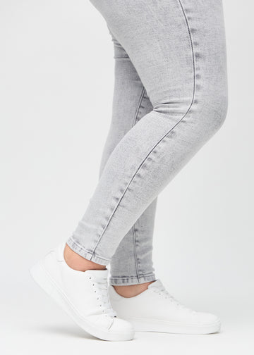 Skinny-Jeans für Damen in Hellgrau, Farbe Ashes. Nahaufnahme der eng anliegenden Beinabschlüsse am Knöchel eines Plus-Size-Models.