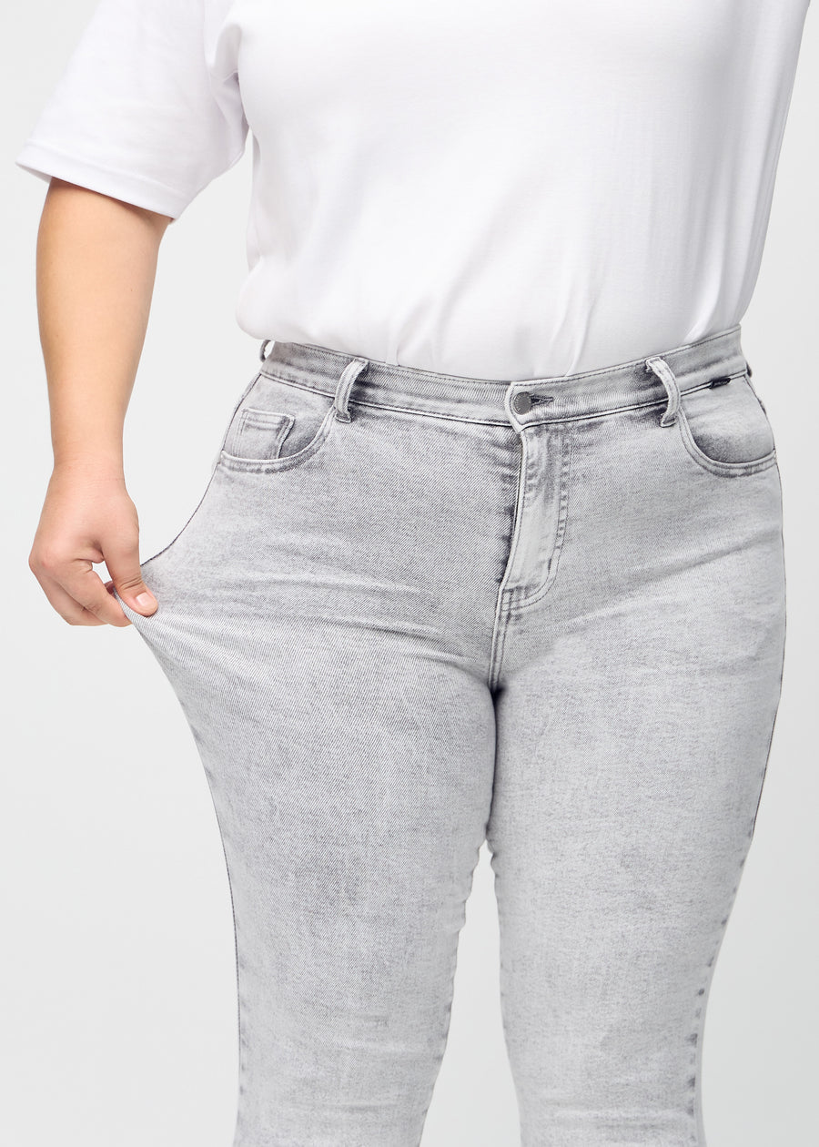 Skinny-Jeans für Damen in Hellgrau, Farbe Ashes. Ein Plus-Size-Model dehnt den Jeansstoff am Oberschenkel, um den Stretch zu zeigen.
