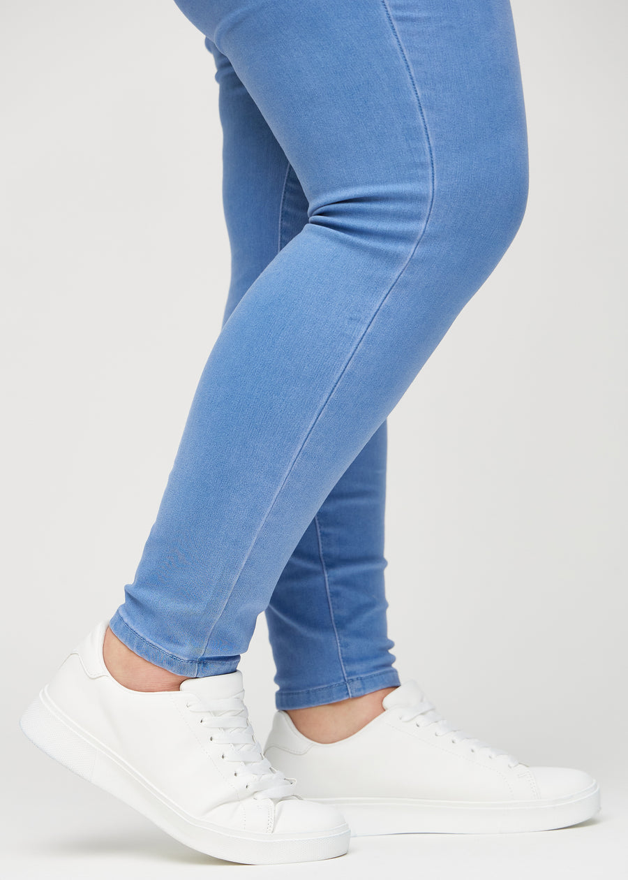 Skinny-Jeans für Damen in Blau, Farbe Geraniums. Nahaufnahme am Knöchel eines Plus-Size-Models, die eng anliegenden Beinabschlüsse sind zu sehen.