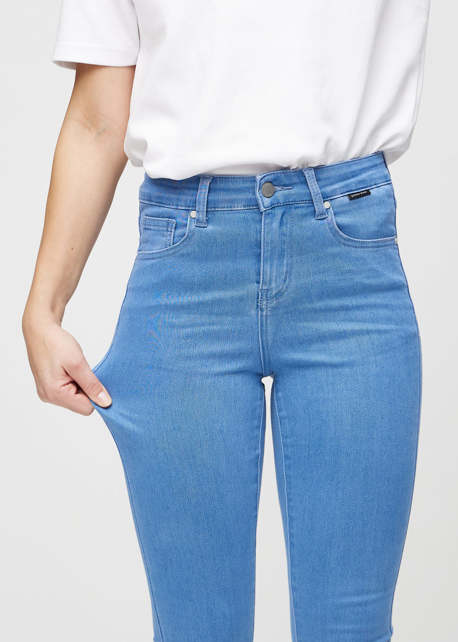 Skinny-Jeans für Damen in Blau, Farbe Geraniums. Ein Model zieht am Jeansstoff am Oberschenkel, um den Stretch zu zeigen.