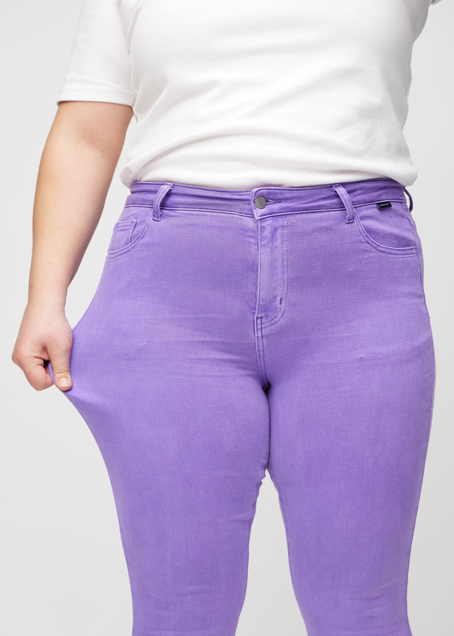 Skinny-Jeans für Damen in Lila, Farbe Lavenders. Ein Plus-Size-Model dehnt den Jeansstoff am Oberschenkel, um den Stretch zu zeigen.