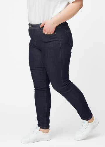 Tief dunkelblaue Denim jeans für Damen in der Farbe Midnights mit skinny Passform, von der Seite an einem Plus-Size-Model gesehen.