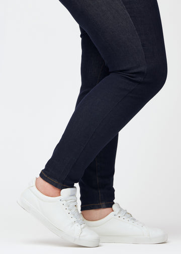 Tief dunkelblaue Denim jeans für Damen in der Farbe Midnights mit skinny Passform in Nahaufnahme an den Knöcheln an einem Plus-Size-Model, um den eng anliegenden Abschluss zu zeigen.