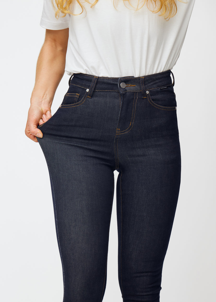 Das Model dehnt die tief dunkelblaue Denim jeans für Damen in der Farbe Midnights am Oberschenkel, um die Elastizität des Materials zu zeigen.