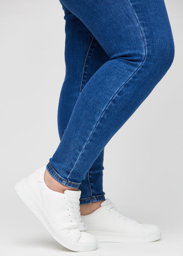 Skinny-Jeans für Damen in Dunkelblau, Farbe Oceans. Nahaufnahme der eng anliegenden Beinabschlüsse am Knöchel eines Plus-Size-Models.