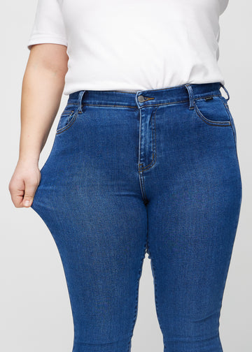 Skinny-Jeans für Damen in Dunkelblau, Farbe Oceans. Ein Plus-Size-Model dehnt den Jeansstoff am Oberschenkel, um den Stretch zu zeigen.