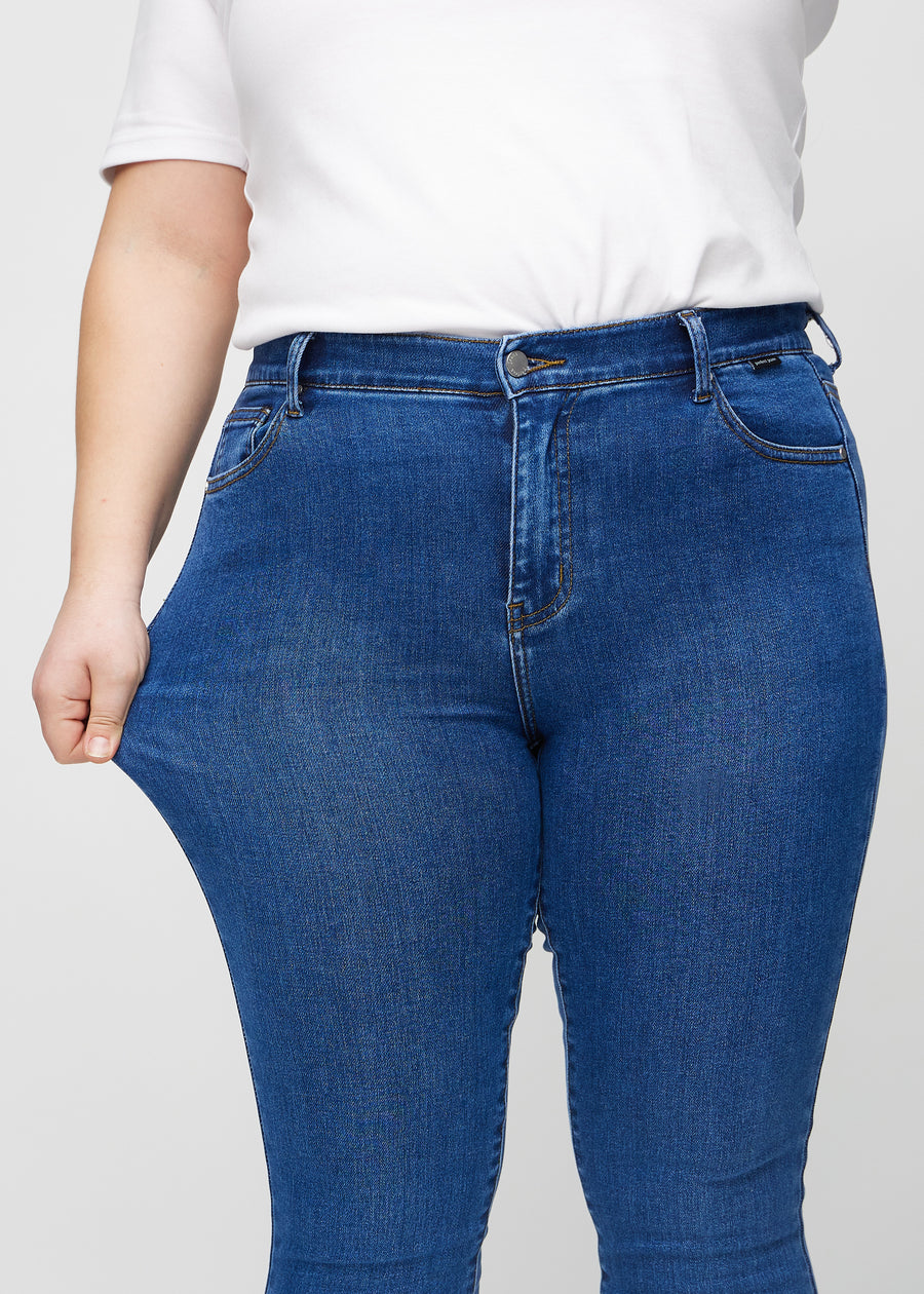 Skinny-Jeans für Damen in Dunkelblau, Farbe Oceans. Ein Plus-Size-Model dehnt den Jeansstoff am Oberschenkel, um den Stretch zu zeigen.