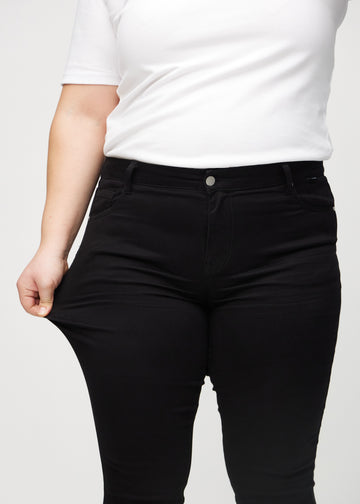 Skinny-Jeans für Damen in Schwarz, Farbe Ravens. Ein Plus-Size-Model zieht am Jeansstoff am Oberschenkel, um den Stretch zu zeigen.