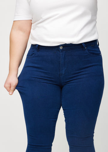 Skinny-Jeans für Damen in Dunkelblau, Farbe Royals. Ein Plus-Size-Model zieht am Jeansstoff am Oberschenkel, um den Stretch zu zeigen.