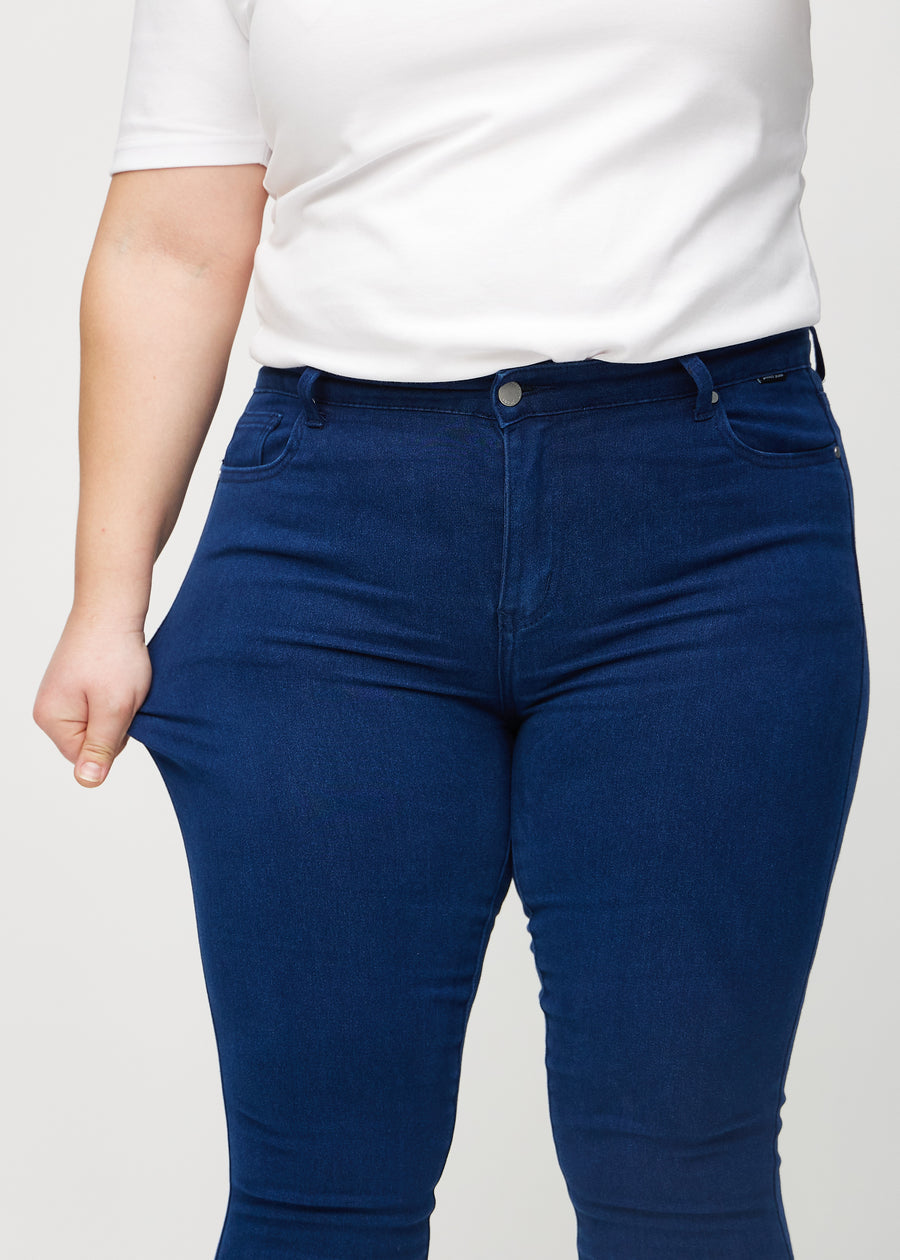 Skinny-Jeans für Damen in Dunkelblau, Farbe Royals. Ein Plus-Size-Model zieht am Jeansstoff am Oberschenkel, um den Stretch zu zeigen.