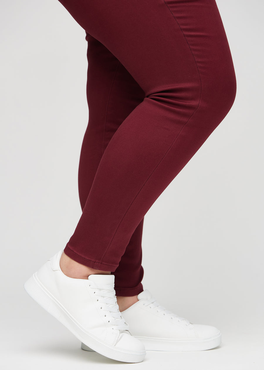 Skinny-Jeans für Damen in Dunkelrot, Farbe Santas. Nahaufnahme der eng anliegenden Beinabschlüsse am Knöchel eines Plus-Size-Models.
