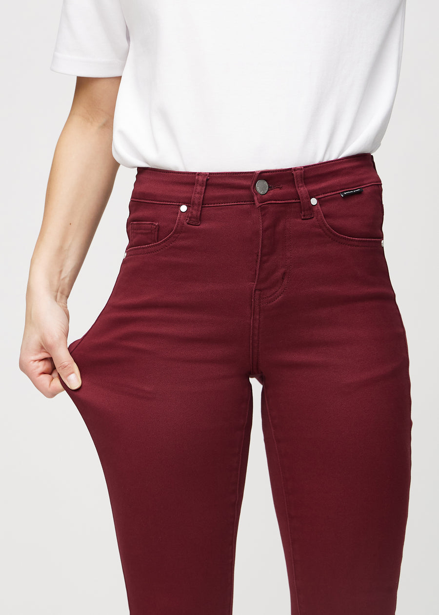Skinny-Jeans für Damen in Dunkelrot, Farbe Santas. Ein Model dehnt den Jeansstoff am Oberschenkel, um den Stretch zu zeigen.