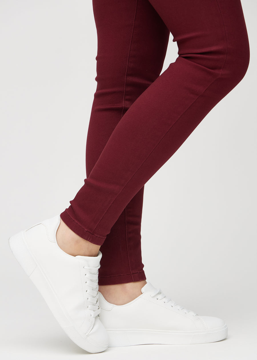 Skinny-Jeans für Damen in Dunkelrot, Farbe Santas. Nahaufnahme der eng anliegenden Beinabschlüsse am Knöchel eines Models.