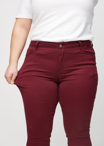 Skinny-Jeans für Damen in Dunkelrot, Farbe Santas. Ein Plus-Size-Model dehnt den Jeansstoff am Oberschenkel, um den Stretch zu zeigen.
