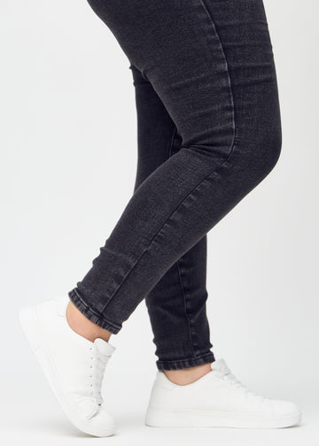 Skinny-Jeans für Damen in Dunkelgrau, Farbe Shadows. Nahaufnahme der eng anliegenden Beinabschlüsse am Knöchel eines Plus-Size-Models.