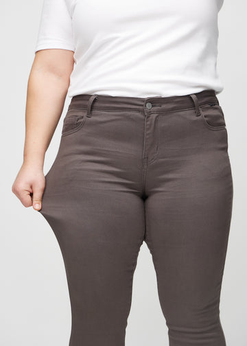 Skinny-Jeans für Damen in Graubraun, Farbe Thunders. Ein Plus-Size-Model dehnt den Jeansstoff am Oberschenkel, um den Stretch zu zeigen.