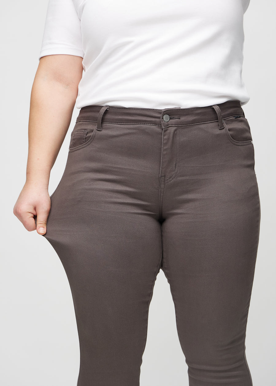 Skinny-Jeans für Damen in Graubraun, Farbe Thunders. Ein Plus-Size-Model dehnt den Jeansstoff am Oberschenkel, um den Stretch zu zeigen.