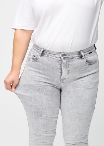 Slim-Jeans für Damen in Hellgrau, Farbe Ashes. Ein Plus-Size-Model zieht am Jeansstoff am Oberschenkel, um den Stretch zu zeigen.
