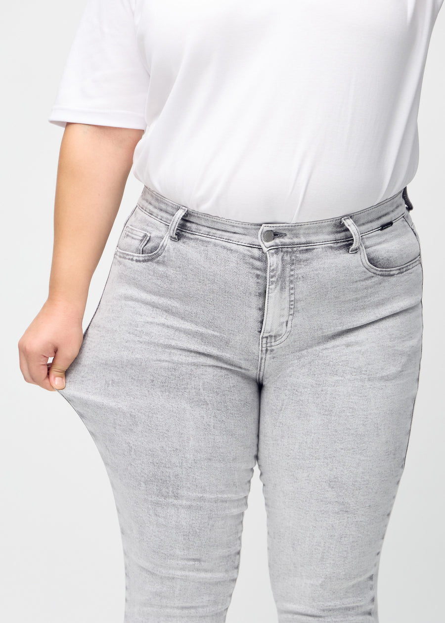 Slim-Jeans für Damen in Hellgrau, Farbe Ashes. Ein Plus-Size-Model zieht am Jeansstoff am Oberschenkel, um den Stretch zu zeigen.
