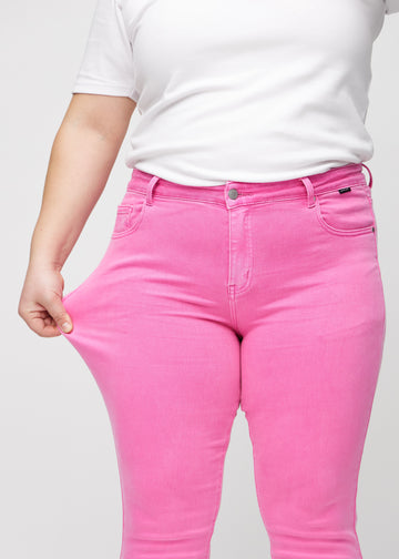 Slim-Jeans für Damen in Hellrosa, Farbe Flamingos. Ein Plus-Size-Model zieht am Jeansstoff am Oberschenkel, um den Stretch zu zeigen.