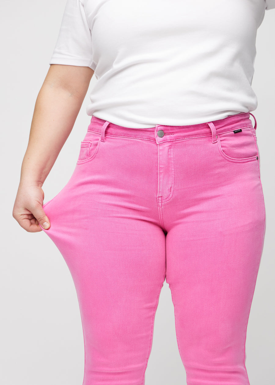 Slim-Jeans für Damen in Hellrosa, Farbe Flamingos. Ein Plus-Size-Model zieht am Jeansstoff am Oberschenkel, um den Stretch zu zeigen.