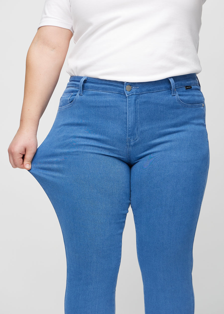 Slim-Jeans für Damen in Blau, Farbe Geraniums. Ein Plus-Size-Model zieht am Jeansstoff am Oberschenkel, um den Stretch zu zeigen.