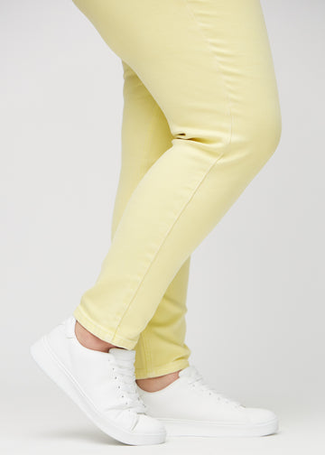 Slim-Jeans für Damen in Hellgelb, Farbe Lemonades. Nahaufnahme an den Knöcheln eines Plus-Size-Models, um die Passform am Beinabschluss zu zeigen.