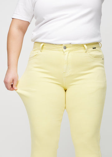 Slim-Jeans für Damen in Hellgelb, Farbe Lemonades. Ein Plus-Size-Model zieht am Jeansstoff am Oberschenkel, um den Stretch zu zeigen.