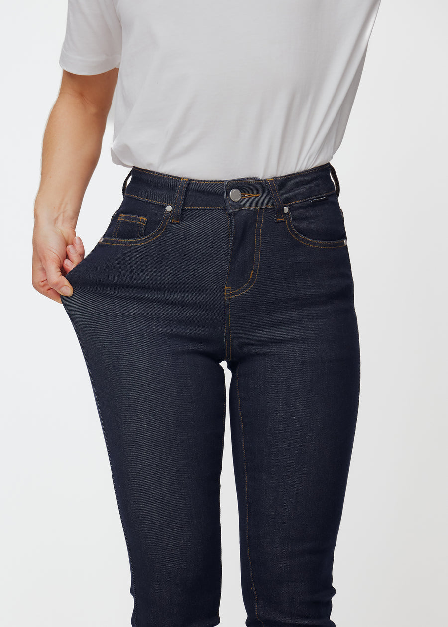 Das Model dehnt die tief dunkelblaue Denim jeans für Damen in der Farbe Midnights am Oberschenkel, um die Dehnbarkeit des Materials zu zeigen.