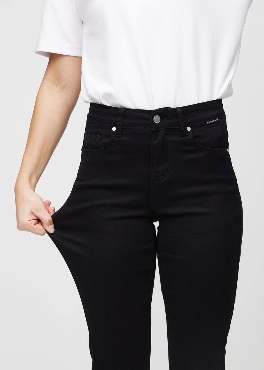 Slim-Jeans für Damen in Schwarz, Farbe Ravens. Ein Model zieht am Jeansstoff am Oberschenkel, um den Stretch zu zeigen.