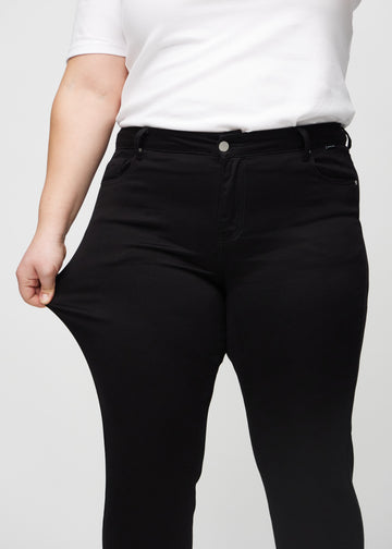 Slim-Jeans für Damen in Schwarz, Farbe Ravens. Ein Plus-Size-Model zieht am Jeansstoff am Oberschenkel, um den Stretch zu zeigen.