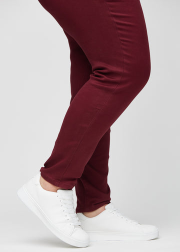 Slim-Jeans für Damen in Dunkelrot, Farbe Santas. Nahaufnahme an den Knöcheln eines Plus-Size-Models, um die Passform am Beinabschluss zu zeigen.