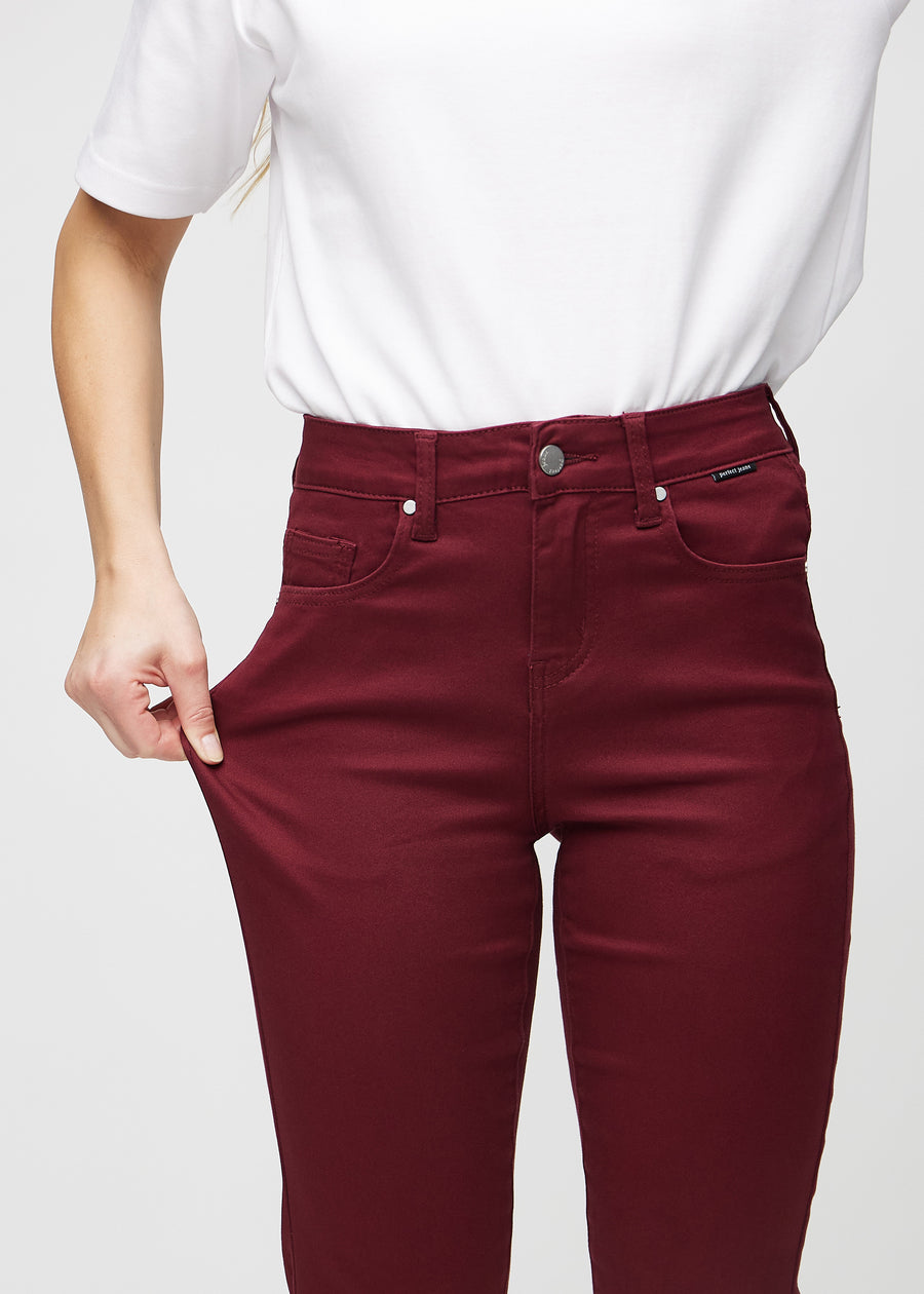 Slim-Jeans für Damen in Dunkelrot, Farbe Santas. Ein Model zieht am Jeansstoff am Oberschenkel, um den Stretch zu zeigen.
