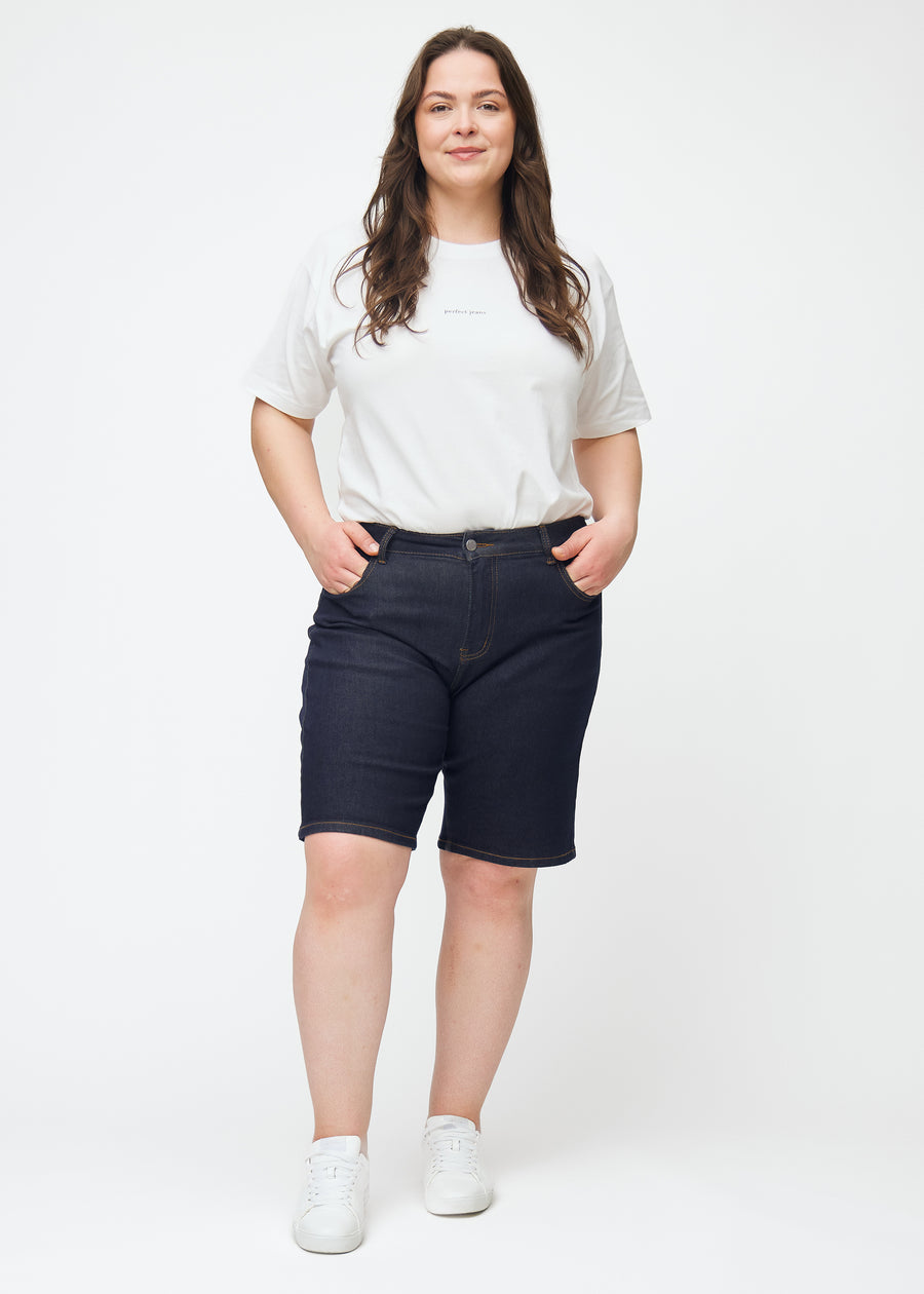 Ganzkörperbild eines Plus-Size-Models in tief dunkelblauen Denim-Shorts für Damen in der Farbe Midnights mit Regular-Passform.
