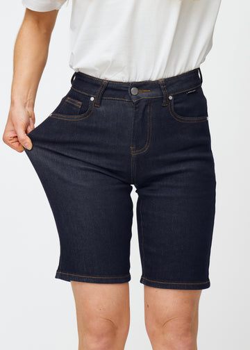 Model dehnt tief dunkelblaue Denim-Shorts für Damen in der Farbe Midnights am Oberschenkel, um den Stretch des Materials zu zeigen.