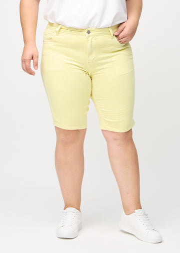 Hellgelbe skinny middle shorts, Modellname Lemonades, die eng am Oberschenkel anliegen und knapp über dem Knie enden, an einem Plus-Size-Model von vorne gesehen.
