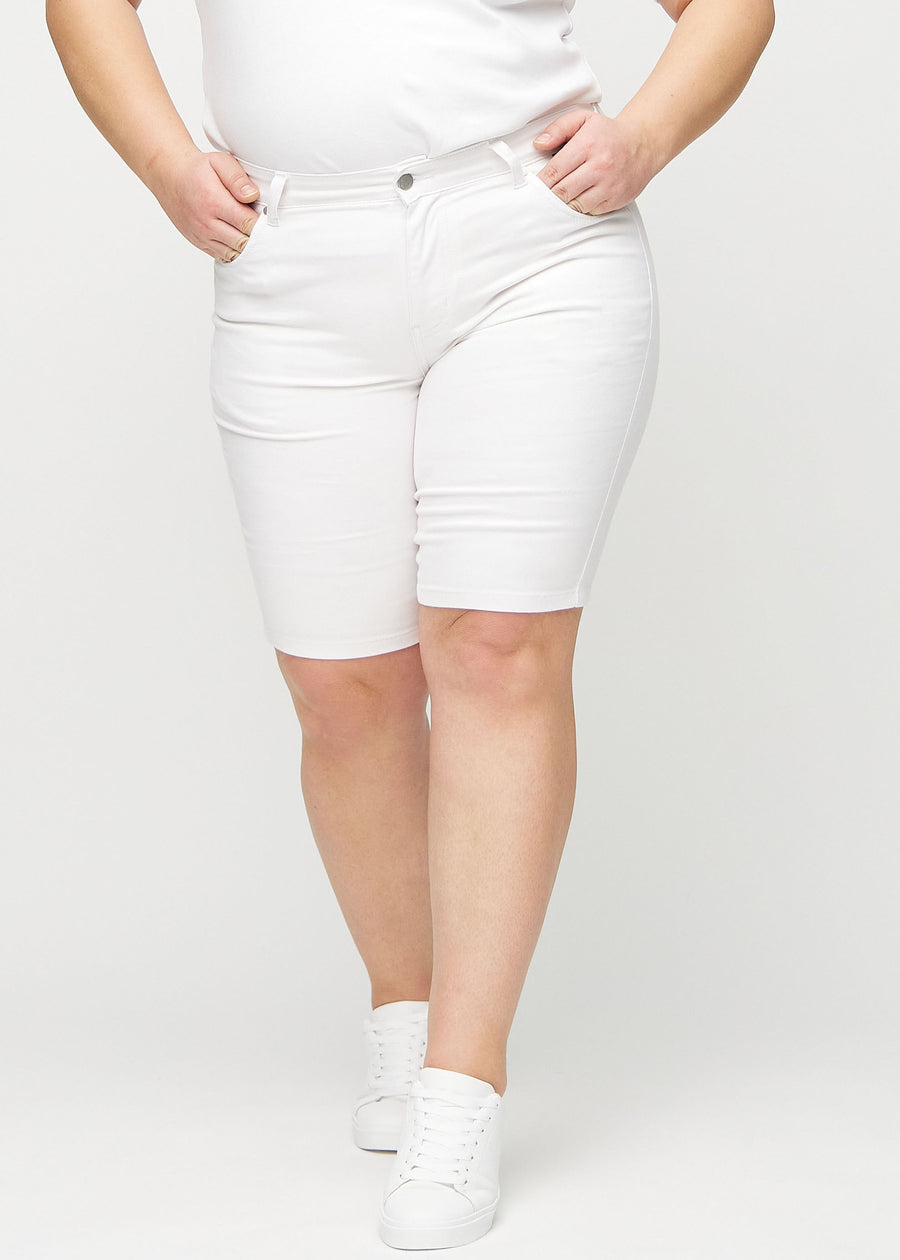 Weiße skinny Middle Shorts, Modellname Marguerites, die eng am Oberschenkel anliegen und knapp über dem Knie enden, an einem Plus-Size-Model von vorne gesehen.