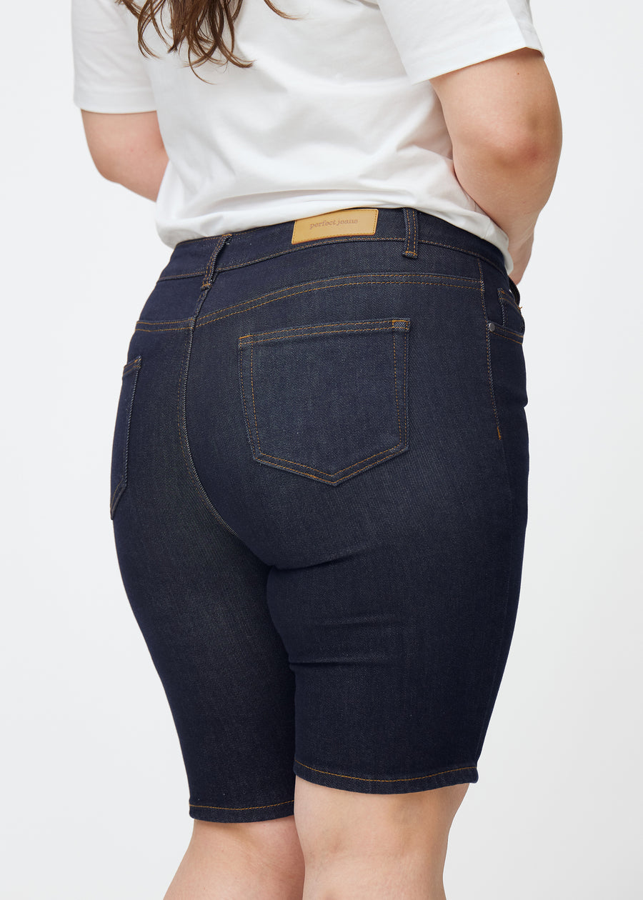 Tief dunkelblaue Denim-Shorts für Damen in der Farbe Midnights von hinten nah auf einem Plus-Size-Model aufgenommen.