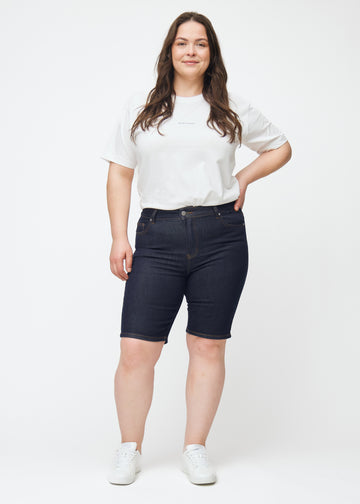 Ganzkörperbild eines Plus-Size-Models in tief dunkelblauen Denim-Shorts für Damen in der Farbe Midnights mit Skinny-Passform.