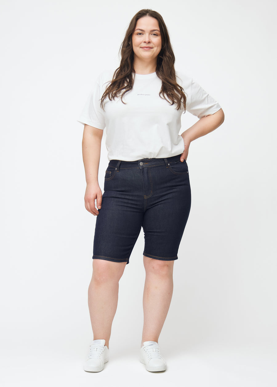 Ganzkörperbild eines Plus-Size-Models in tief dunkelblauen Denim-Shorts für Damen in der Farbe Midnights mit Skinny-Passform.