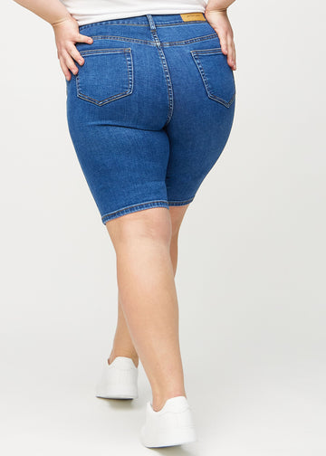 Dunkle Denim-skinny middle shorts von hinten an einem Plus-Size-Model gesehen, sodass man das gesamte Produkt sehen kann.