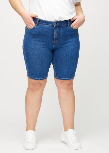 Dunkle Denim-skinny middle shorts, Modellname Oceans, die eng am Oberschenkel anliegen und knapp über dem Knie enden, an einem Plus-Size-Model von vorne gesehen.