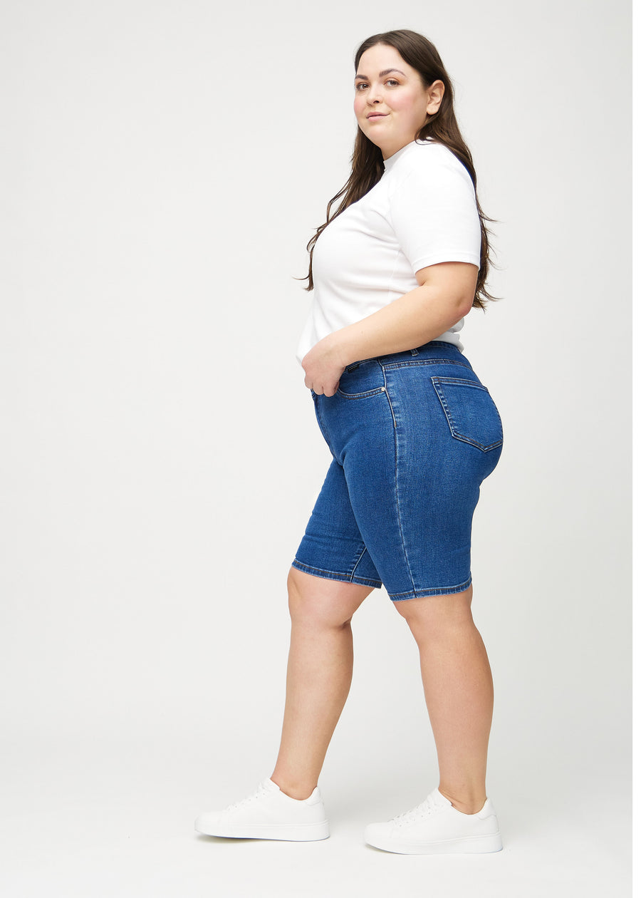 Dunkle Denim-skinny middle shorts von der Seite an einem Plus-Size-Model gezeigt.