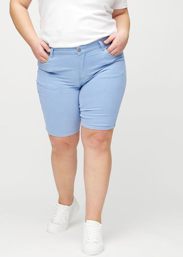 Hellblaue skinny middle shorts, Modellname Skies, die eng am Oberschenkel anliegen und knapp über dem Knie enden, an einem Plus-Size-Model von vorne gesehen.