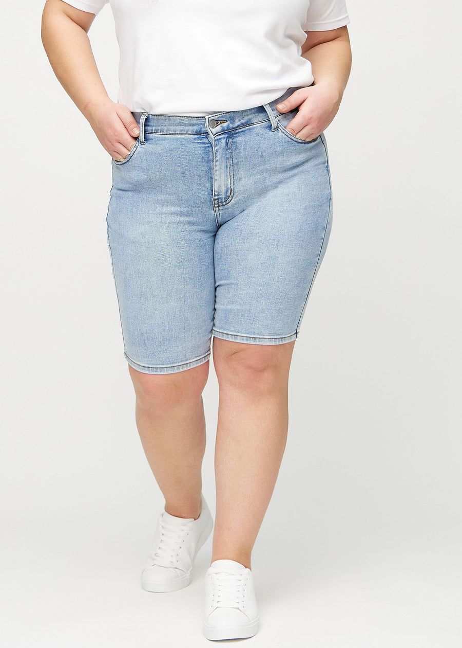 Helle Denim-skinny Middle Shorts, Modellname Waves, die eng am Oberschenkel anliegen und knapp über dem Knie enden, an einem Plus-Size-Model von vorn gesehen.