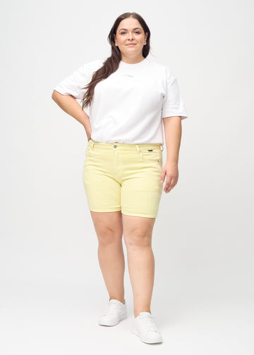 Ganzkörperbild eines Plus-Size-Models in hellgelben skinny Short Shorts.